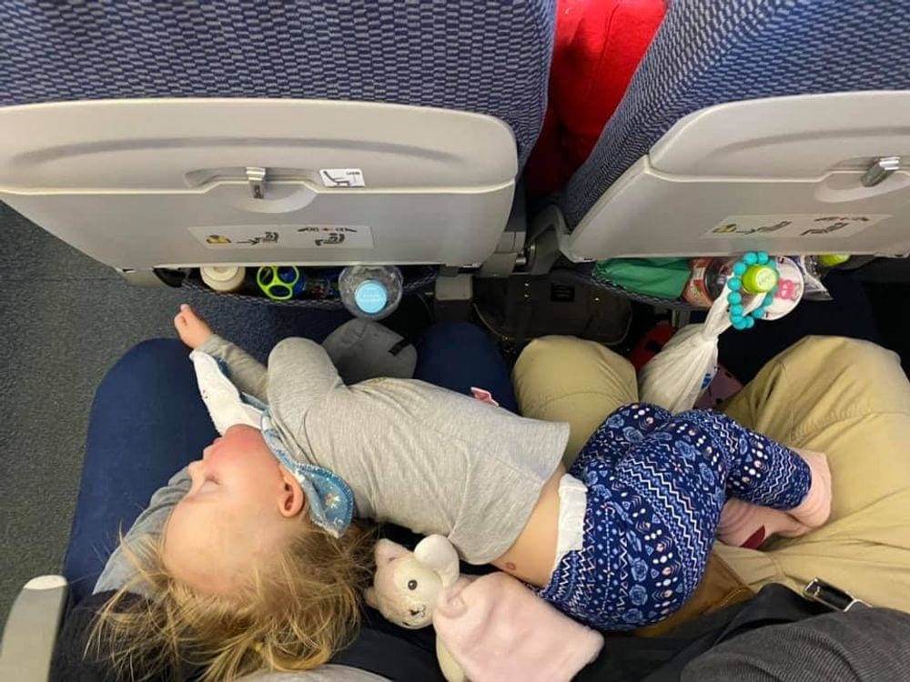 An infant sleeps across the laps of her parents mid-flight.