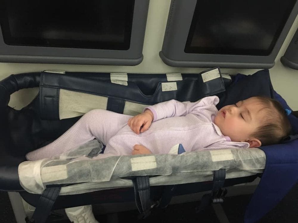 An infant girl sleeps in an on-board bassinet mid-flight.