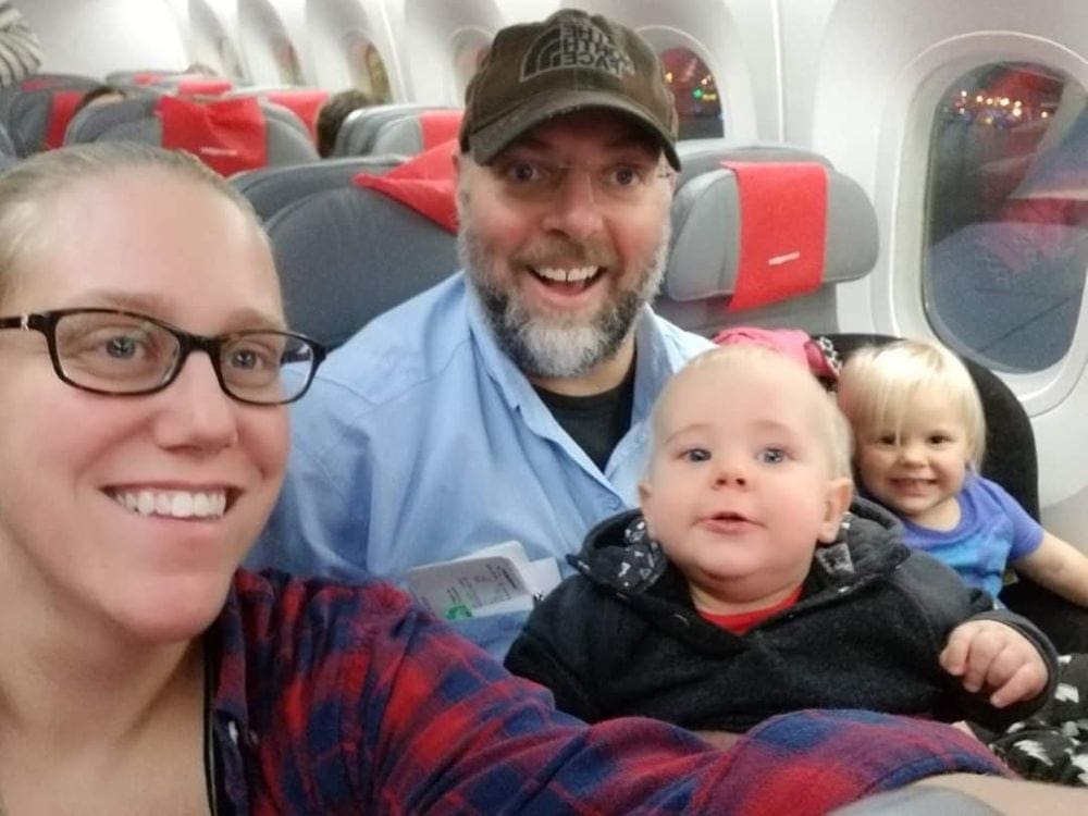 A family of four smiles as the mom takes a selfie inside an airplane before embarking on their journey.