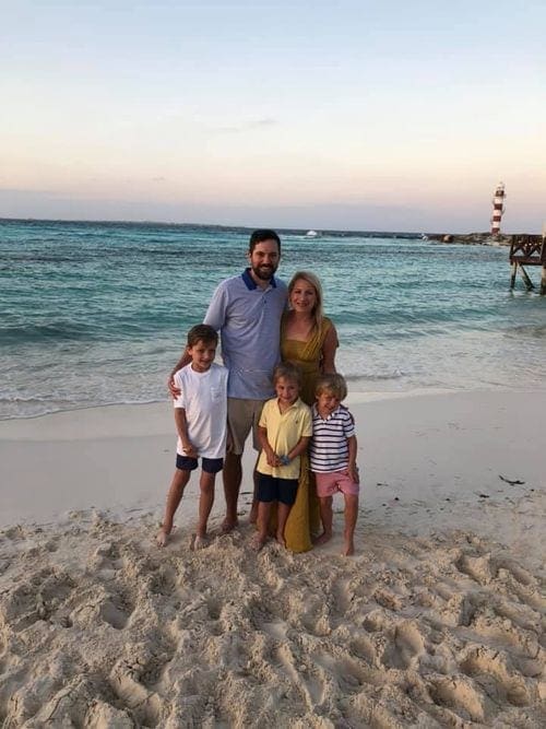 A family of five stands smiling on a beach in Cancun, a red and white lighthouse stands in the background.