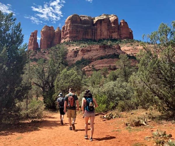 Three people hike along a trail with Sedona's iconic red rocks in the distance near Sedona, Arizona, one of the best places to visit in the US during Easter Break with kids!