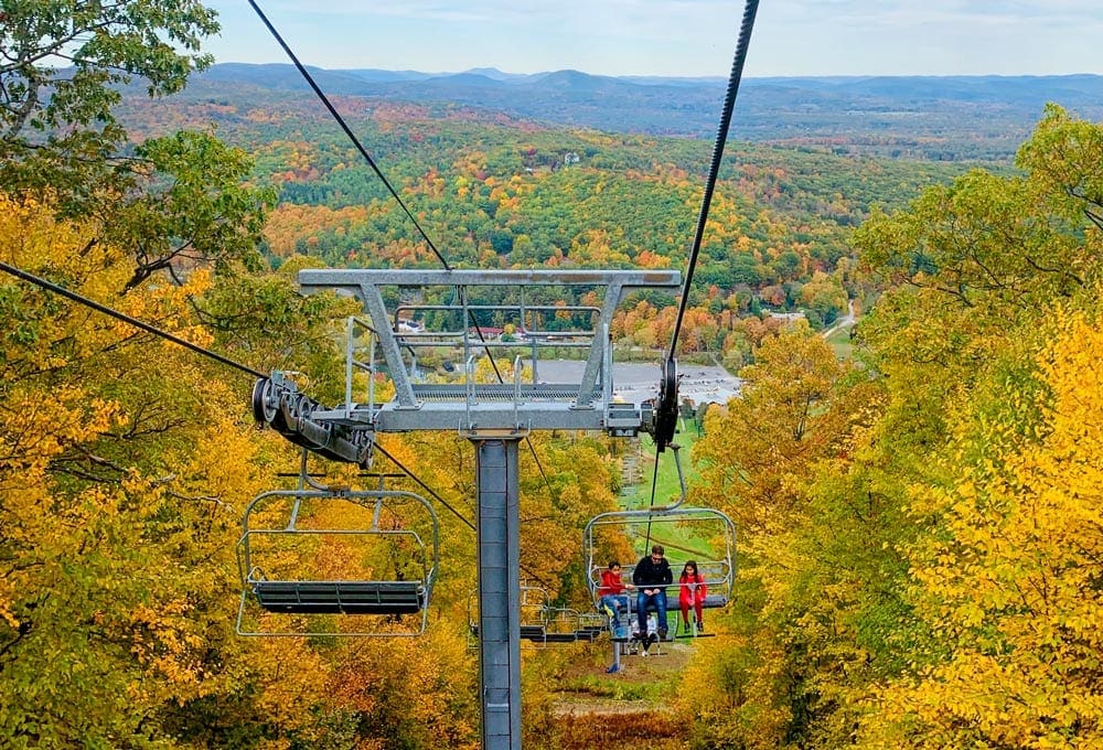 A ski chair hold an adult and two children amongst sweeping views of the golden fall foliage in Massachusetts.