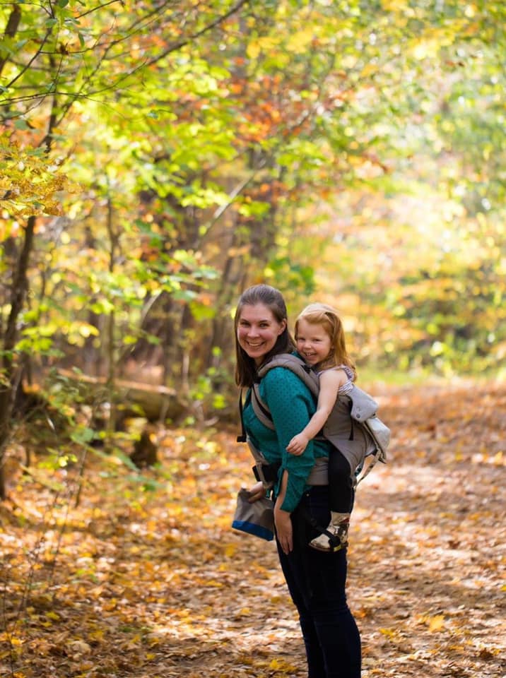 A young girl rides on her mothers back during a brightly colored fall hike in Vermont.