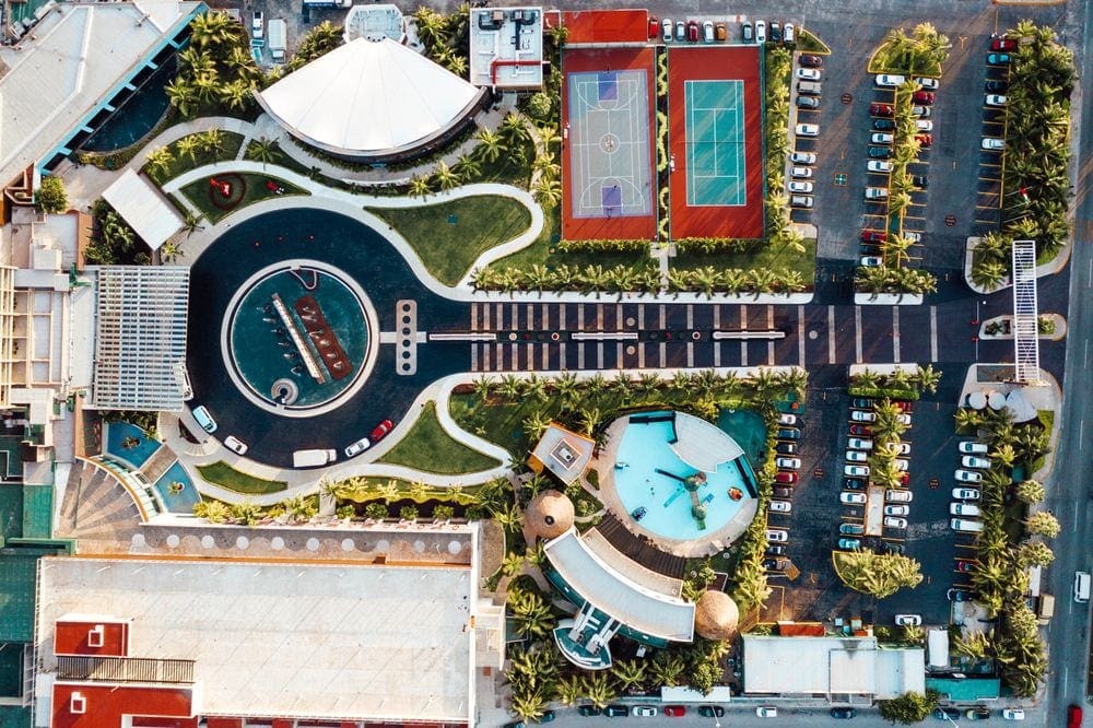 An ariel view of the Hard Rock Hotel Cancun, featuring a guitar shaped entrance and water feature. From the areiel view, you can see the parking lot, building, pool, and athletic courts, as well.