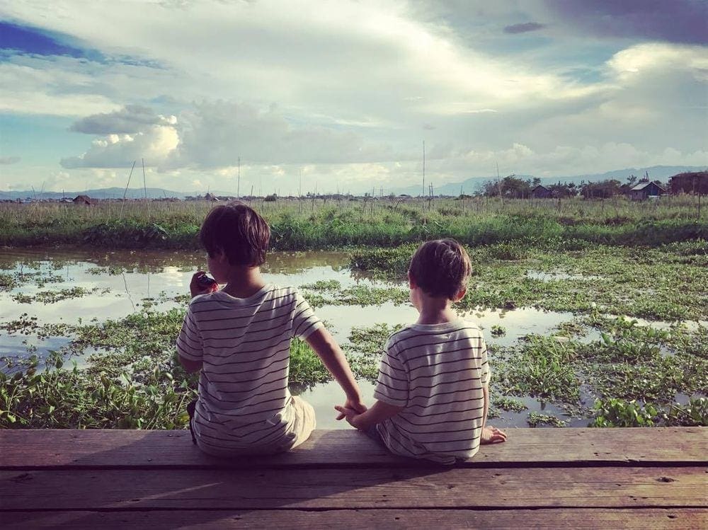 Two young boys hold hands while looking out at a field in Vietnam.