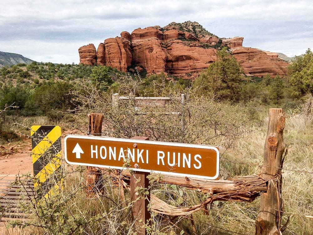 A picture of the red rock landscape featuring a Honanki Ruins sign, pointing to the Honanki Heritage Site, one of the best things to do in Sedona for families. 