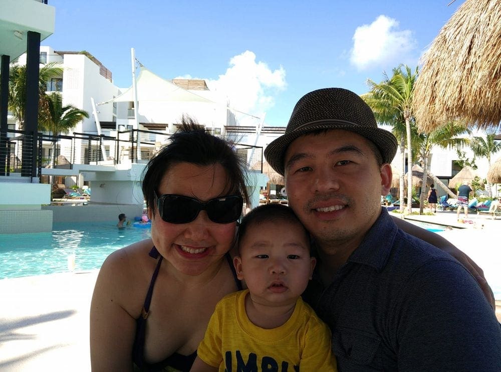 A fmaily of three smiles while enjoying a sunny day near the pool at Finest Playa Mujeres in Cancun, staying in a family friendly hotel is one of the best tips for traveling with a toddler.