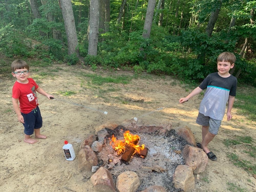 Two boys stand on opposite sides of a bonfire roasting marshmallows, one of the best things to do when camping in the Shenandoah River Valley with Kids.