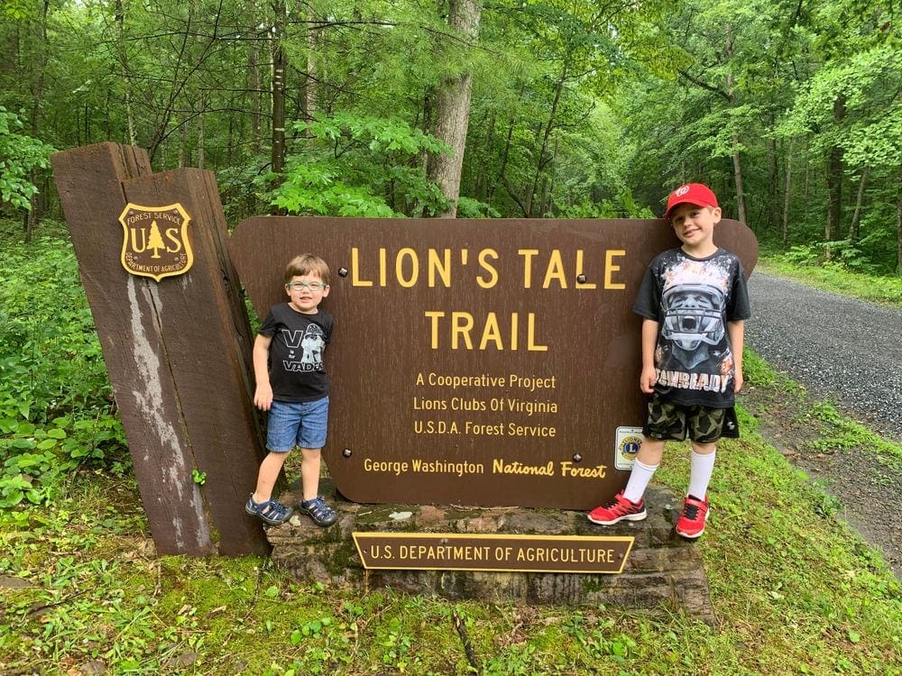 Two boys flank the entrance sign for Lion's Tale Trail, part of George Washington National Forrest in Virginia, one of the best things to do in the Shenandoah River Valley with Kids.