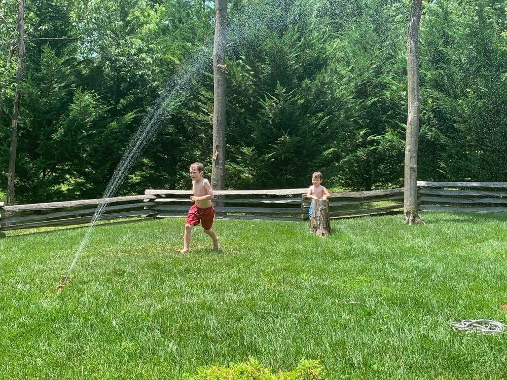 Two boys run through a large spray of water coming from a sprinkler, while visiting the Shenandoah River Valley as a family.