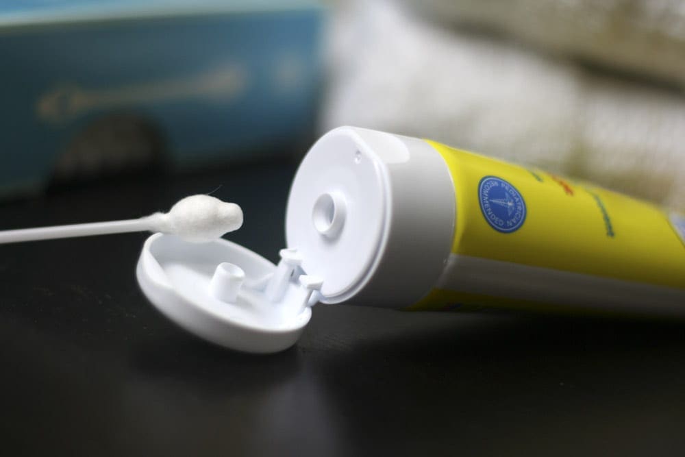 A q-tip with a small dap of white ointment rests against the lid of a tube of ointment.