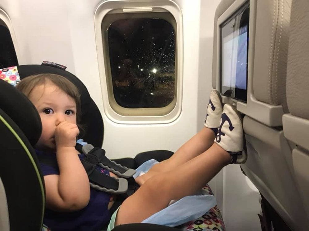 Part of our Frontier Airlines kids policies article, this is an infant girl suck her thumb while sitting in a carseat on a plane preparing to take off. 