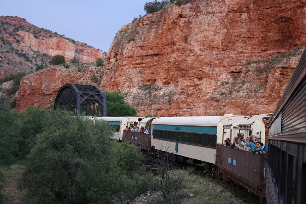 A view of the Verde Canyon Train, which is one of the best things to do in Sedona for families, as it veers around the iconic Red Rocks. Several train cars are pictured, including two open air cars.