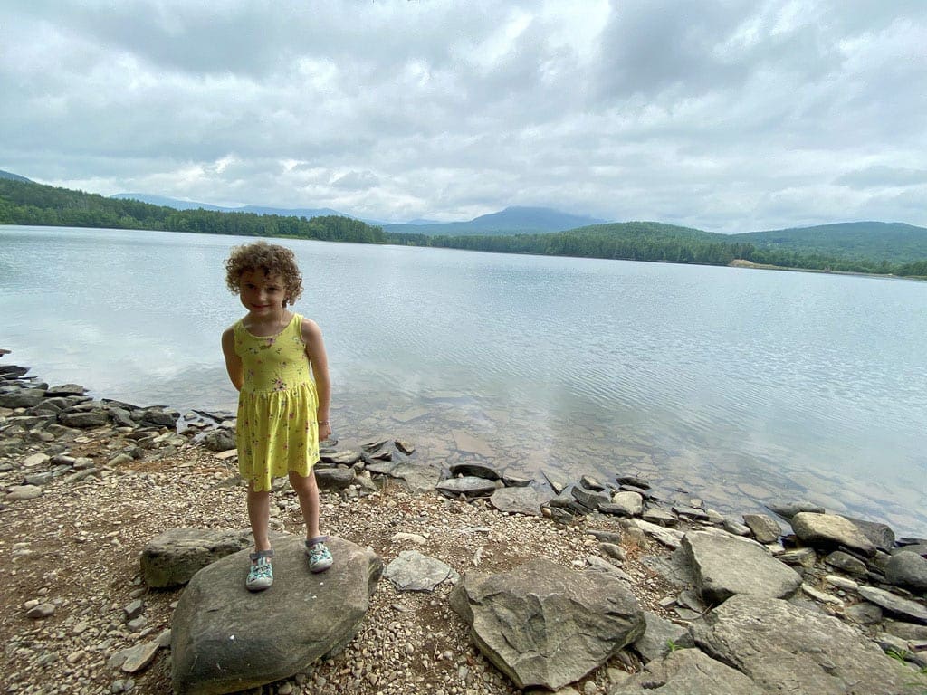 A young girl in a yellow dress stands proudly in front of Cooper Lake, offering one of the best kid-friendly hikes in the Hudson Valley.