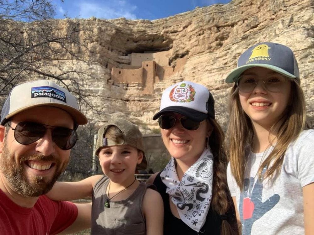 A family of four, all wearing hats, takes a selfie in front of Montezuma Castle, one of the best things to do in Sedona for families.