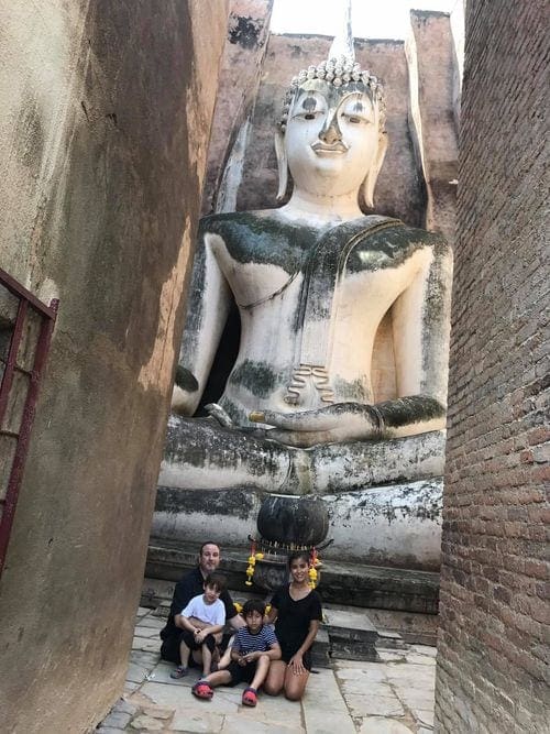 A family of four sits beneath a huge Buddha statue.