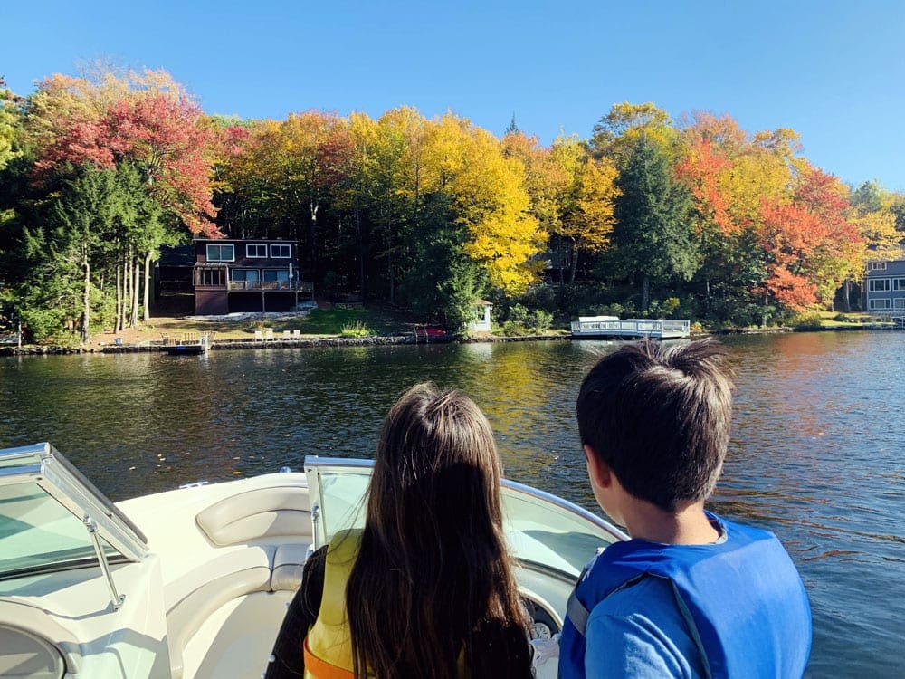 A young boy and girl look toward a stunning fall scene across a lake from the boat they are riding in.