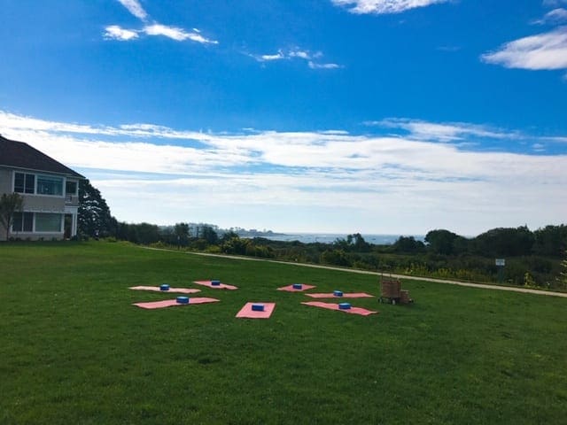Several yoga mats are circled around an open space on the grass in preparation for an outdoor class.