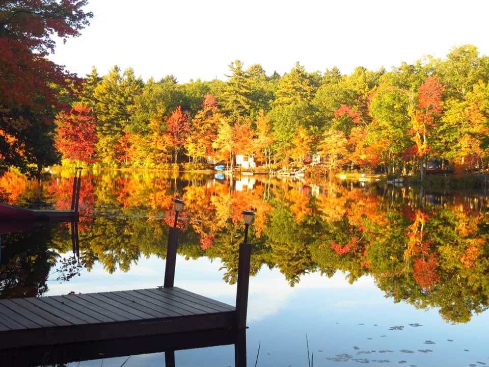 A dock sticks out into a glimmering lake on a charming and colorful autumn day in New Hampshire.