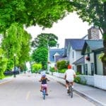 A young girl and her father bike along an enchanting, tree-lined streen on Mackinac Island, Michigan, one of the most charming towns to visit with kids.