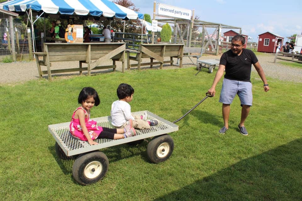 A dad pulles his two children on a wagon through Alstede Farms, one of the best places for apple picking with kids near NYC.