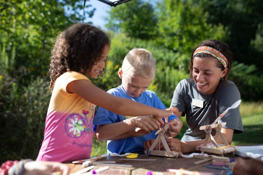 A counselor works with two kids as they make a craft in the kid's program at Smuggler's Notch Resort, one of the best Vermont hotels for families.