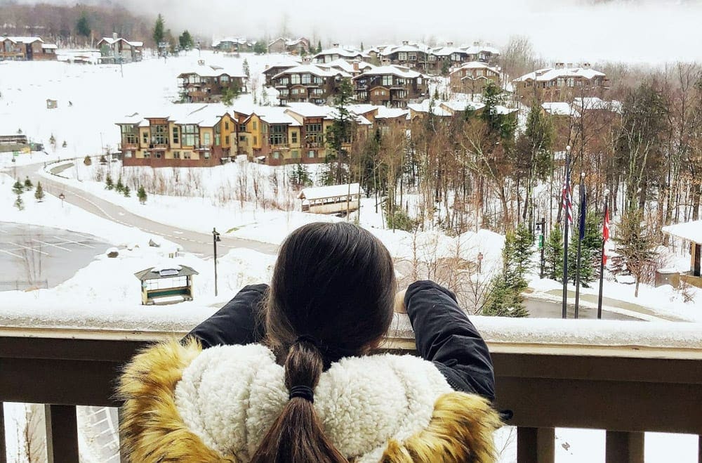 A young girl looks over the railing out at the Lodge at Spruce Peak on a winter day.