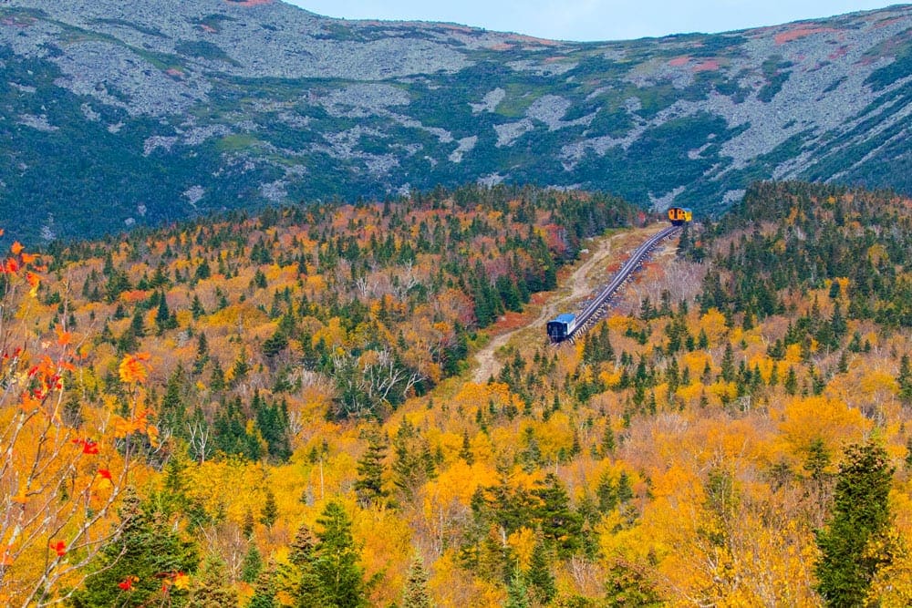 The Mount Washington Cog Railway car ascends to the sumit in an array of fall colors, a great option for a fall foliage train ride in the Northeast.