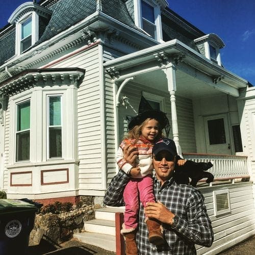 A dad holds his daughter on his shoulder while standing in front of one of the iconic houses used in the Hocus Pocus movies in Salem.