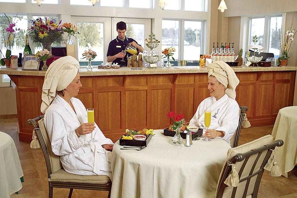 Two women sit laughing while enjoying mimosas at the restaurant on-site at Stoweflake Mountain Resort & Spa, one of the best Vermont hotels for families.