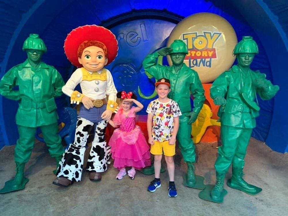 A young girl and boy pose with Jessie and three arm soldiers within Toy Story Land at WDW.