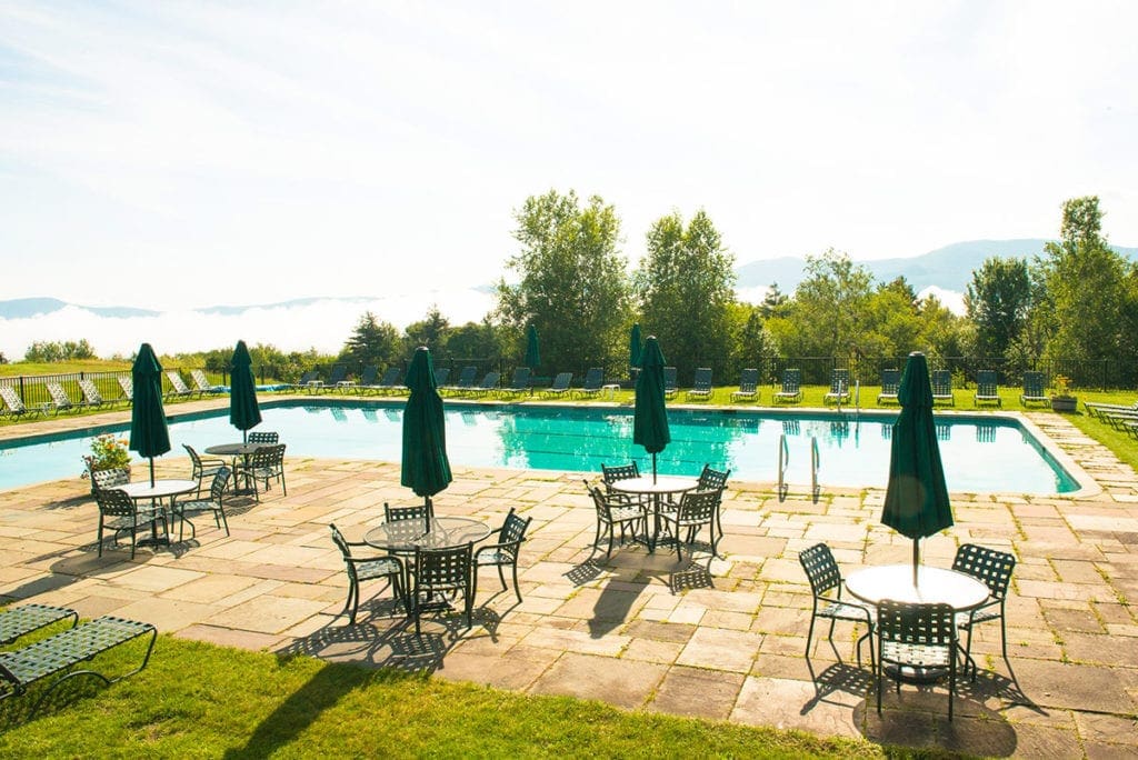 Several tables with chairs sit next to a tranquil pool at the Trapp Family Lodge.