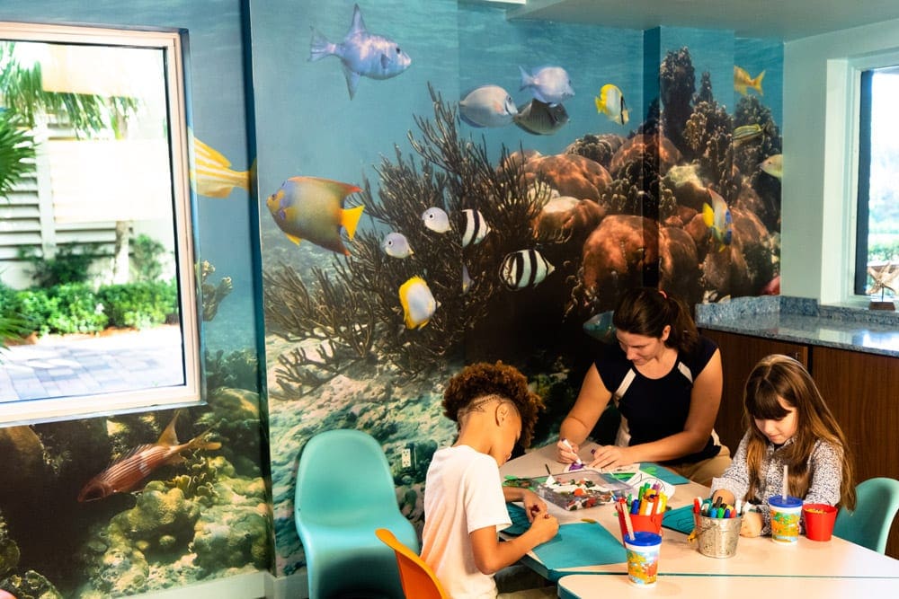 Two children color with a child care attendant at the kids club in The Acqualina Resort.