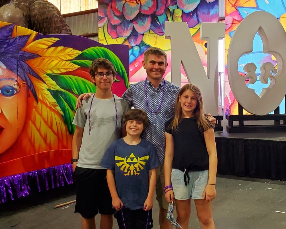 A dad stands with his three kids inside Mardi Gras World in New Orleans, one of the best vacation spots in the US to impress teens and tweens.