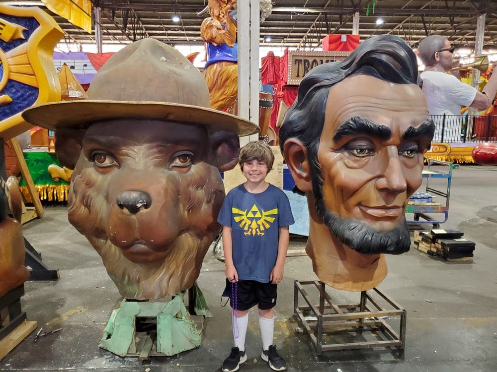 A young boy stands between the head of Smokey the Bear and Abraham Lincoln, both used in a Mardi Gras parade, now houses at the Mardi Gras Museum.