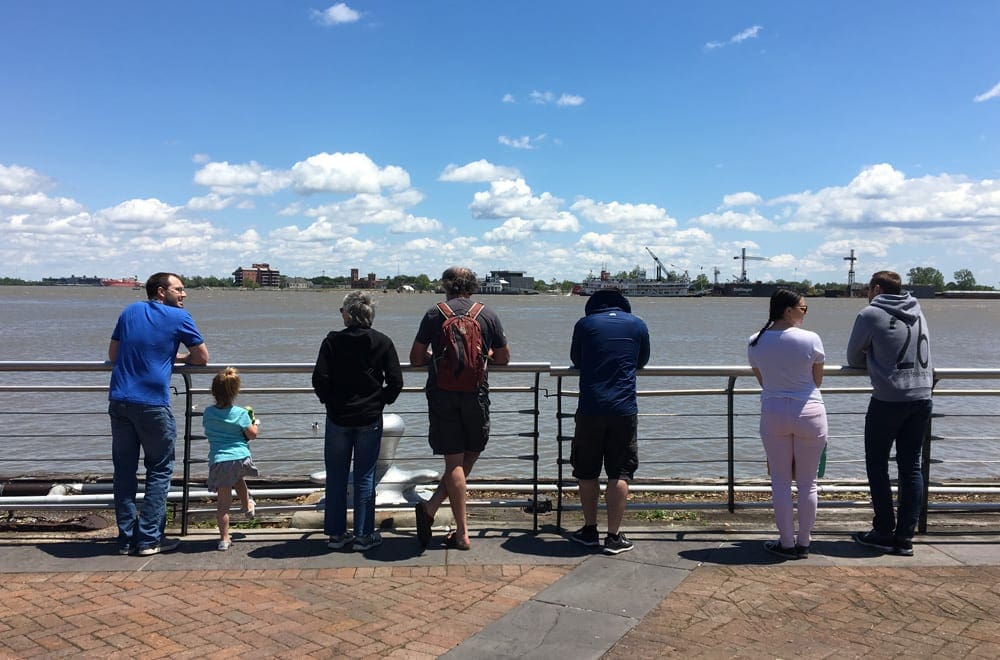 A family of 7 leans against a railing looking at the Mississippi River in New Orleans.