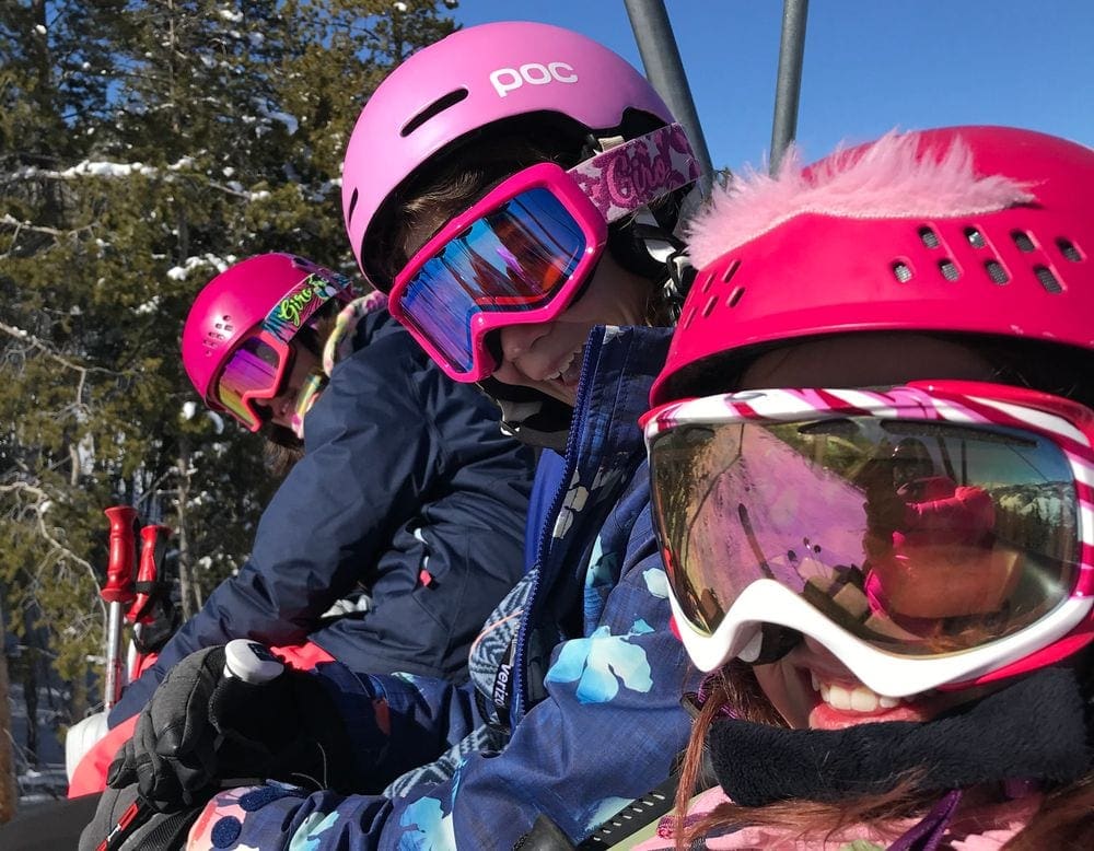 Three skiers wearing bright pink helmets and goggles go skiing in Vail in the winter with kids.
