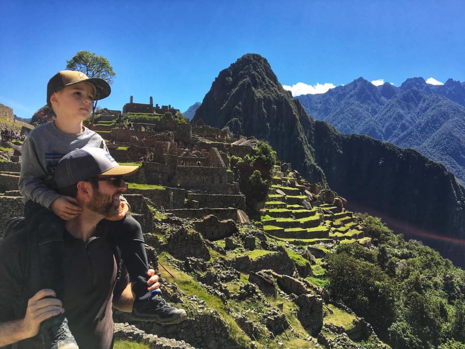 A young boy sits on his dad's shoulders as they look onto Macchu Picchu.