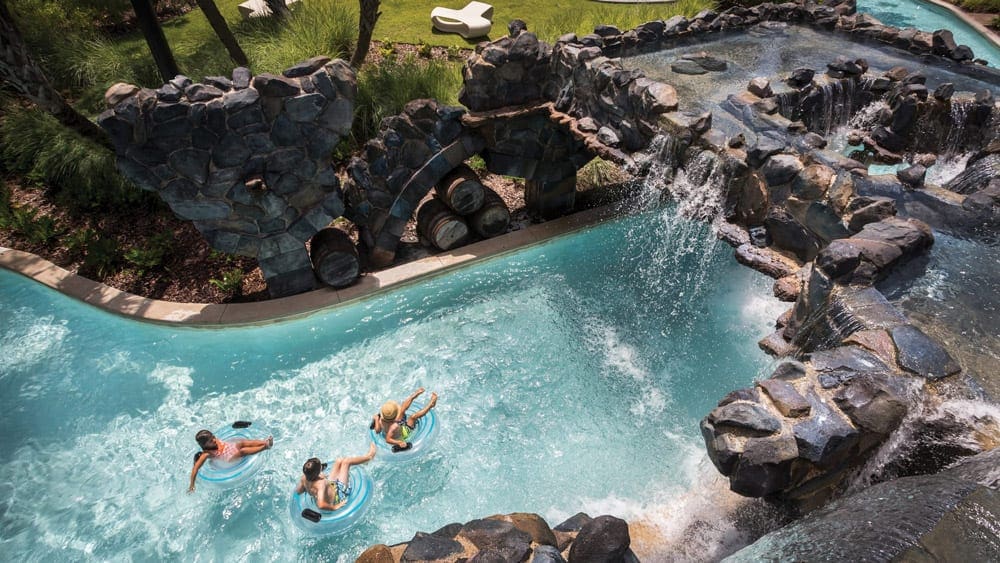 Three people float down the lazy river on-site at Four Seasons, Orlando, on large flotation tubes.