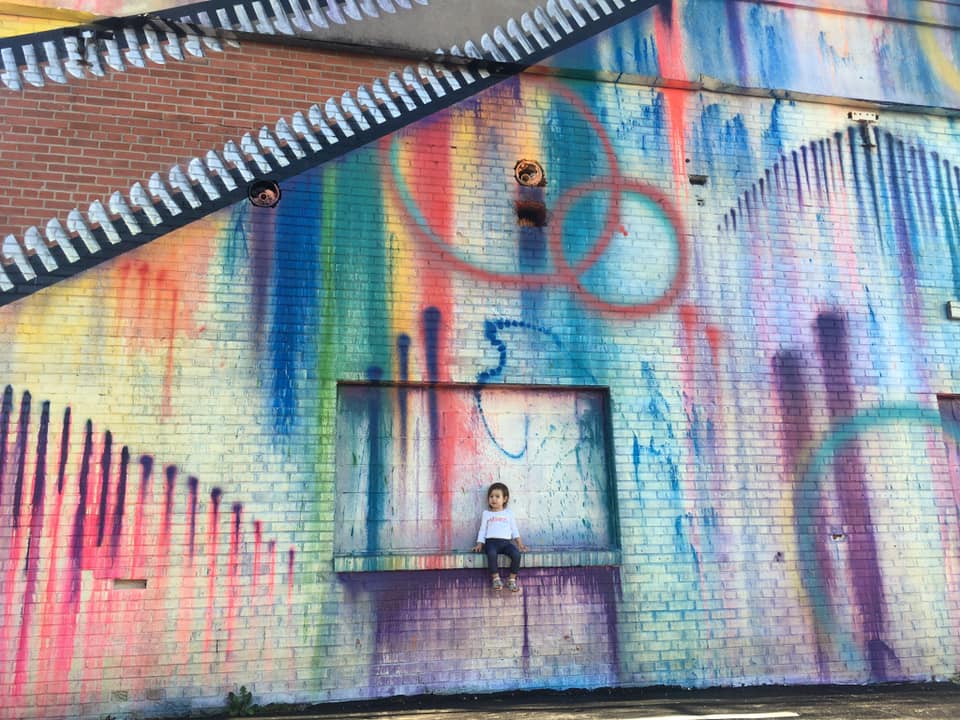 A young child sits high on a ledge surrounded by street art in Houston.