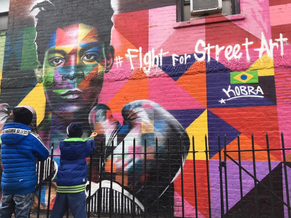 Two boys look on at a mural in NYC, featuring a black boxer, a colorful background, and the words "#Fight For Street Art".