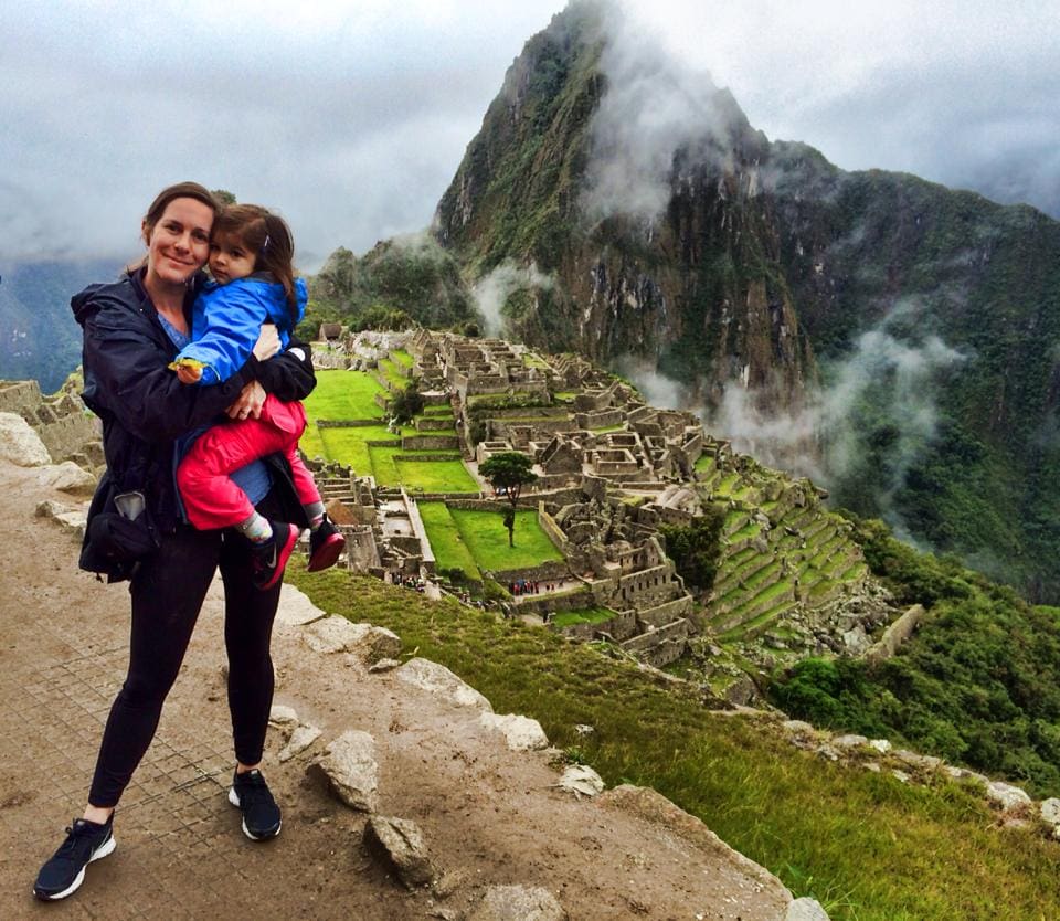 A mom stands holding her young daughter with Machu Picchu in the background.