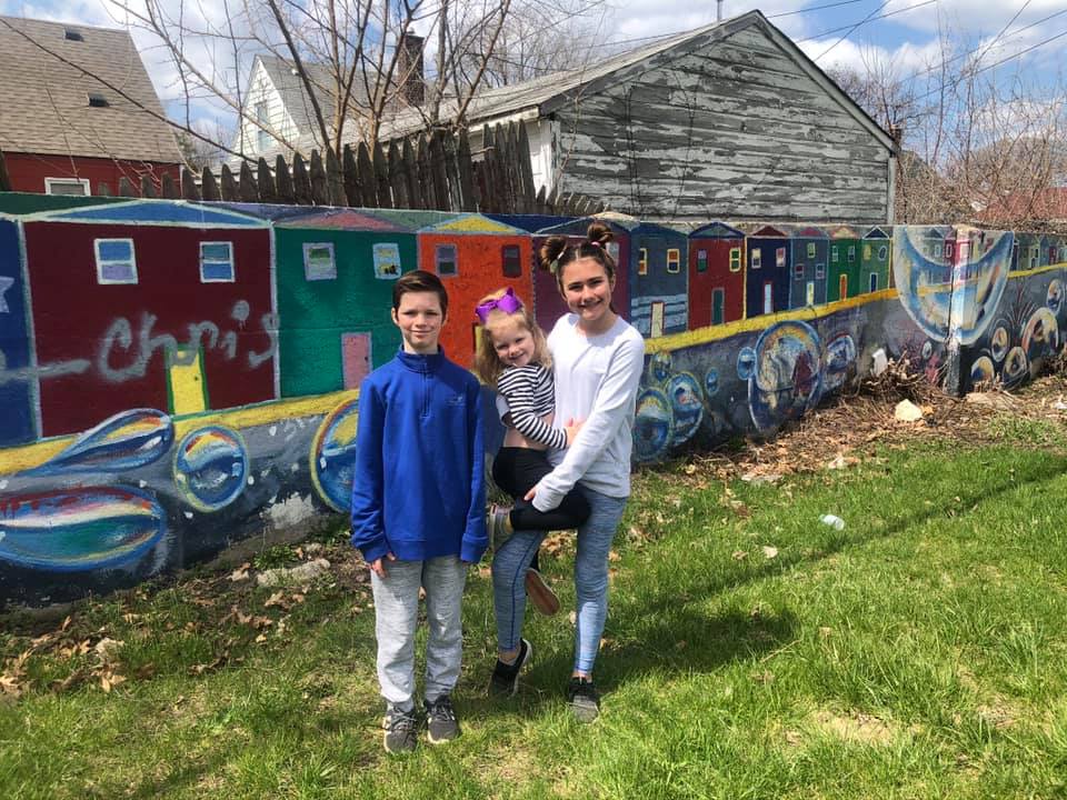 A family of three stands in front of colorful street art in Detroit, one of the best places to visit in Michigan with kids.