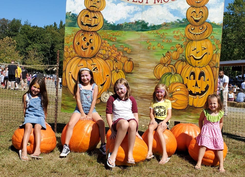 Five kids sit on large pumpkins in front of a sign at Harvest Moon Farms, one of the best pumpkin patches near NYC to visit with kids.