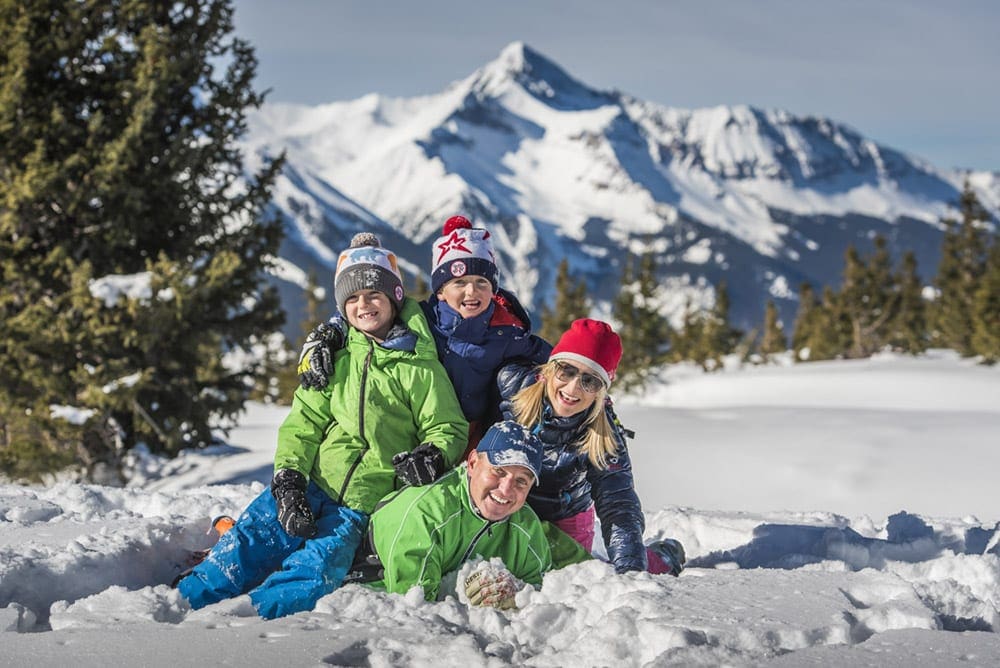 A family of four wearing snow gear piles in the snow at Telluride.