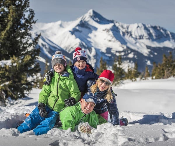 A family of four wearing snow gear piles in the snow at Telluride.