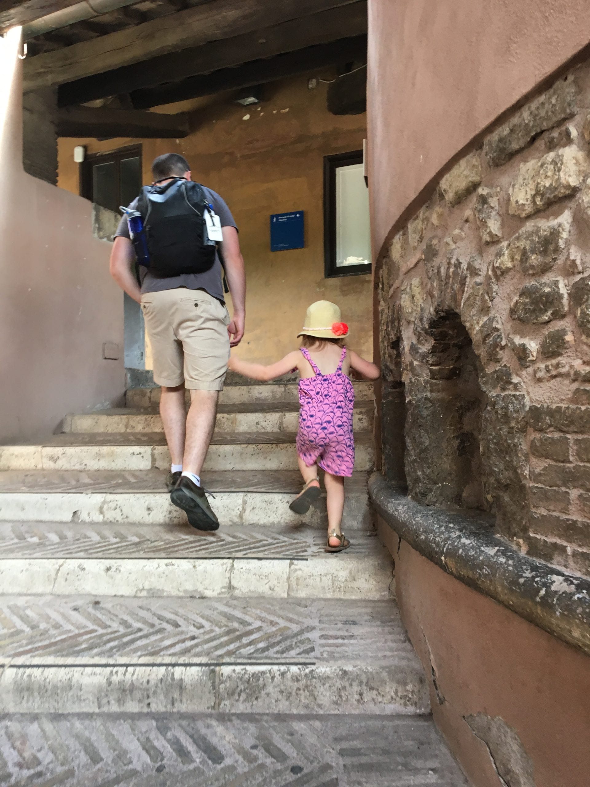 A dad holds his young daughter's hand as they walk up the stairs within Castel Sant'Angelo.