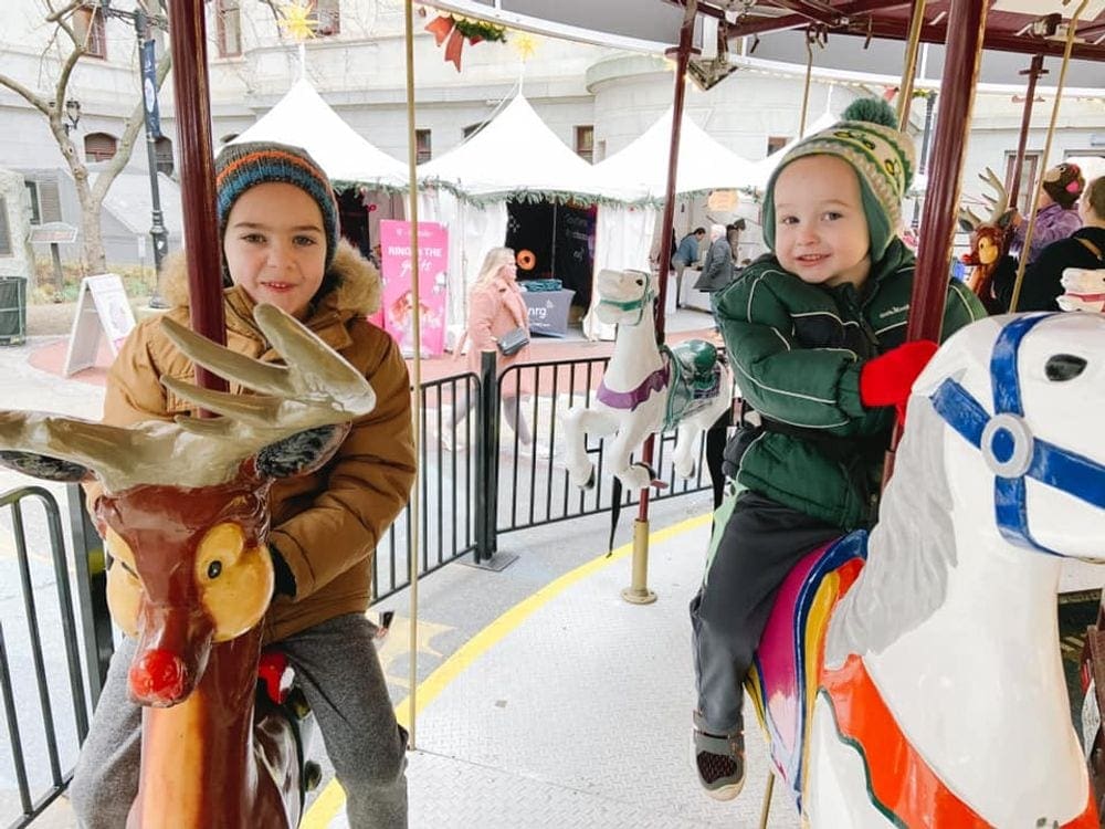 Two kids ride a festive carousel inside a Christmas market in Philadelphia, one of the best Christmas towns in the Northeast.