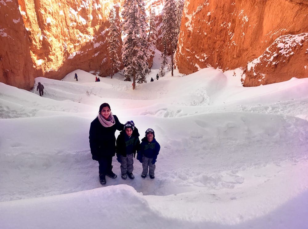 A parent and two small children wearing winter gear stand in the snow within Bryce Canyon National Park, one of the best national parks in Winter with kids.