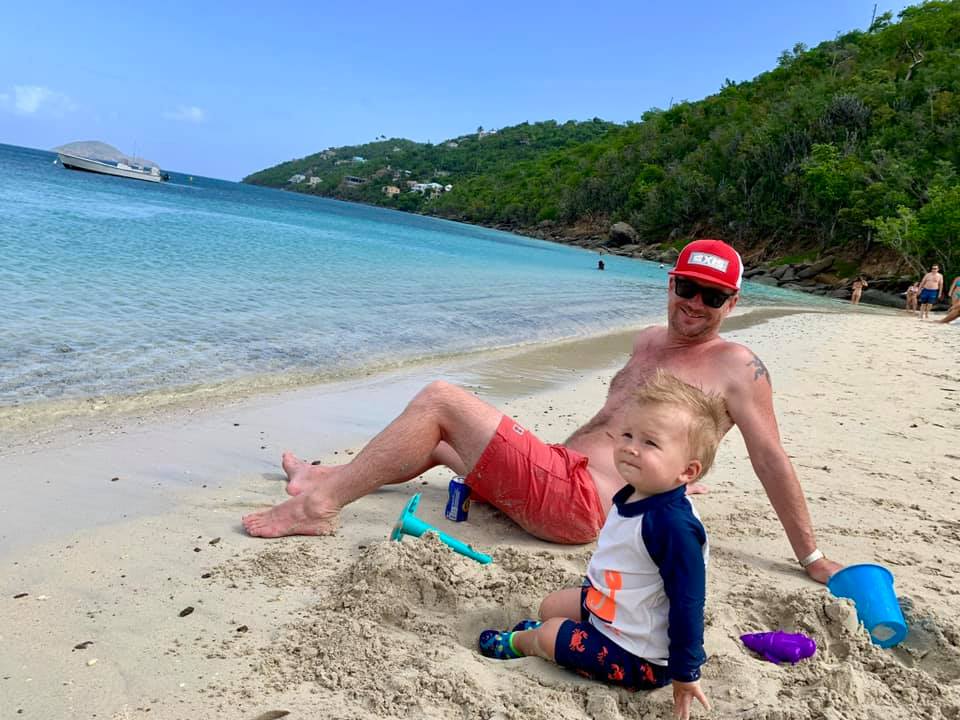 A dad and son sit on a beach in St. Thomas on a sunny day.